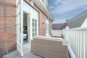 A patio area with a wicker sofa, a white fence, and a brick wall. - Fletcher Nautisch Kwartier (Huizen)