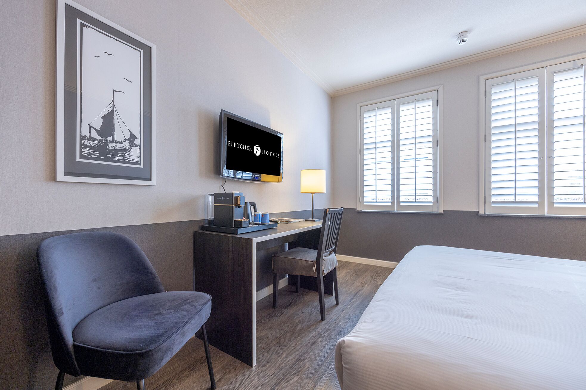 Habitación de hotel con una cama, un escritorio con computadora, una silla, un televisor y una ventana con persianas.