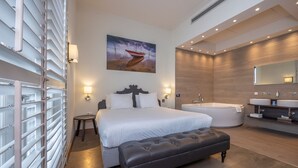A modern bedroom with a large bed, a bench, a painting, a bathtub, and a bathroom with a mirror and sink. - Fletcher Nautisch Kwartier (Huizen)