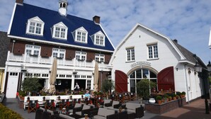 A building with a blue tiled roof and a white facade, featuring a sign that reads "Riva Wine Lounge." - Fletcher Nautisch Kwartier (Huizen)