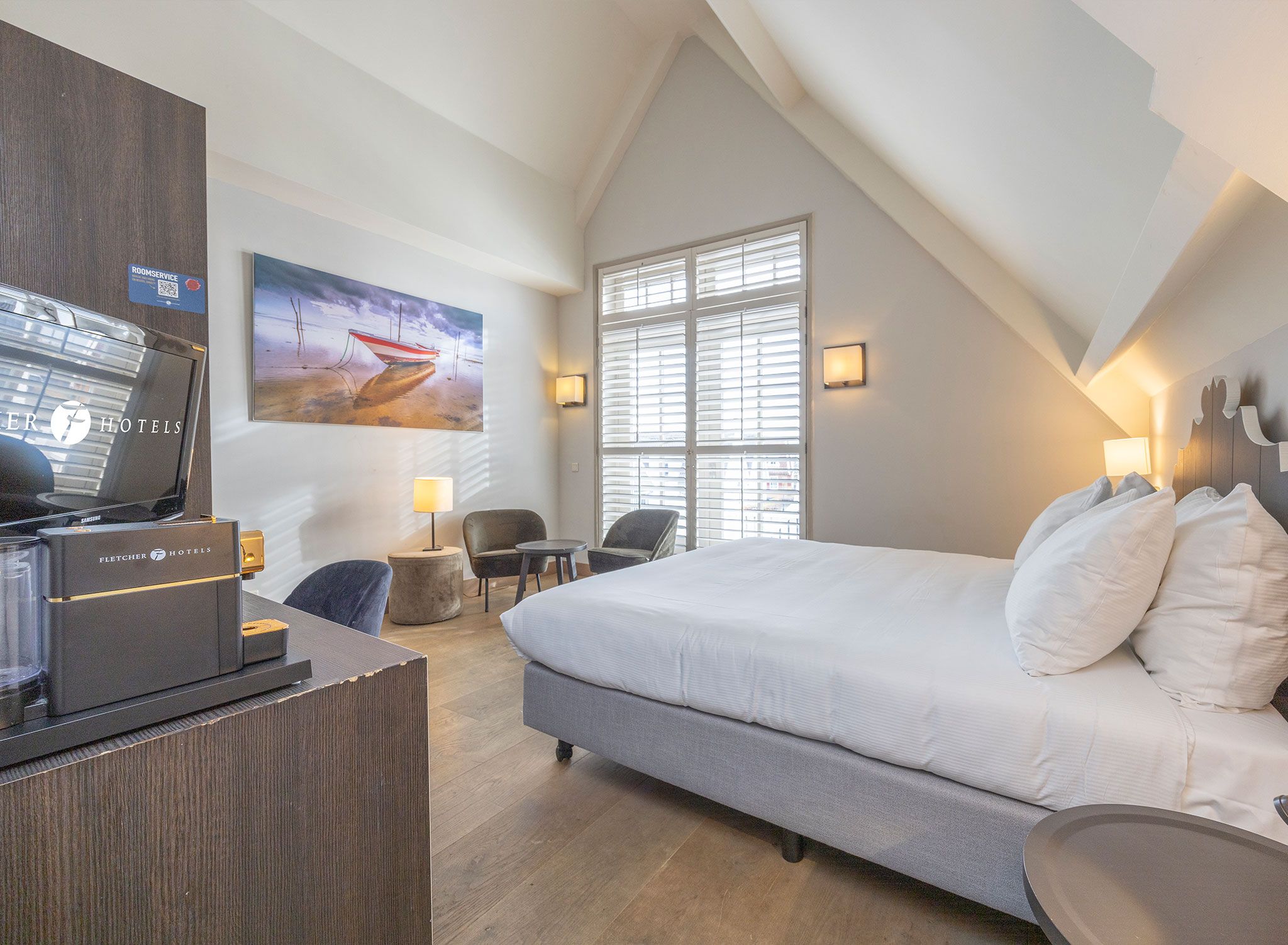 Habitación de hotel con cama, escritorio, sillas y un cuadro.