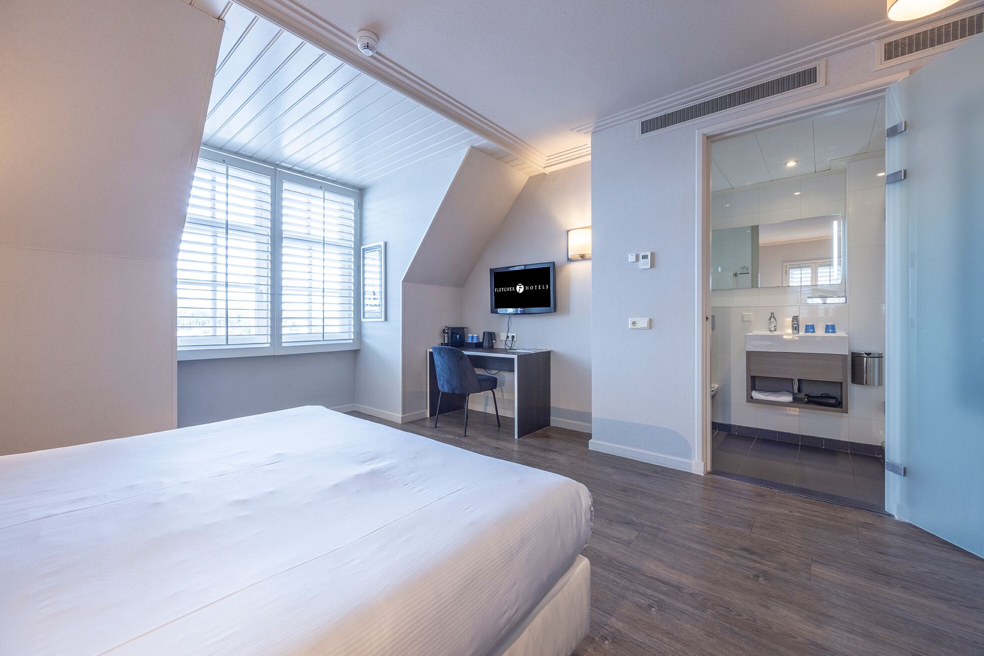 Une chambre d’hôtel moderne dotée d’un grand lit, d’un bureau, d’une télévision et d’une salle de bain avec un miroir et un lavabo.