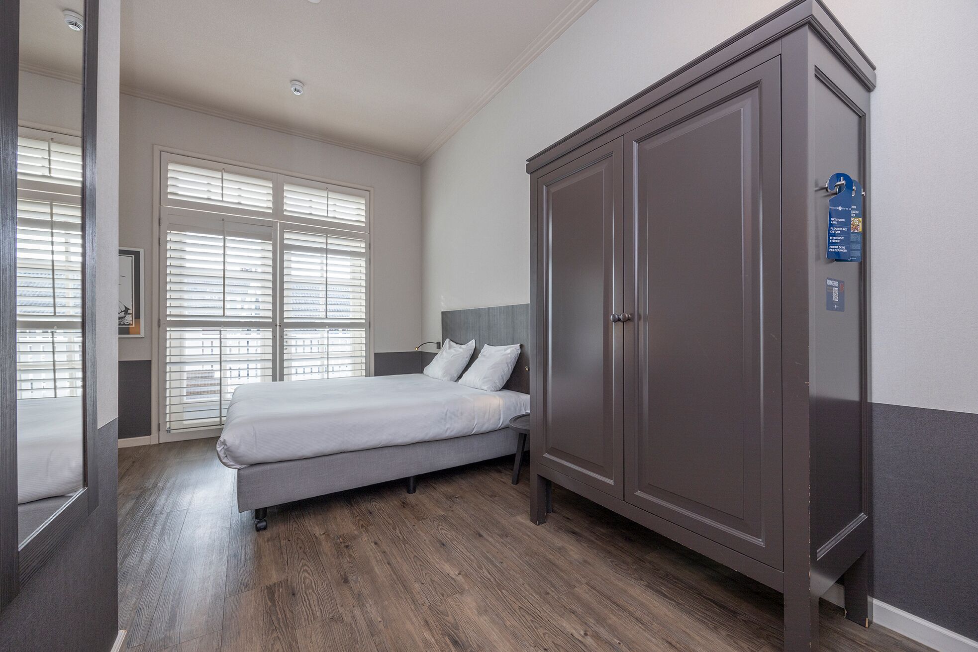 A hotel room with a bed, a wardrobe, and a window with blinds.