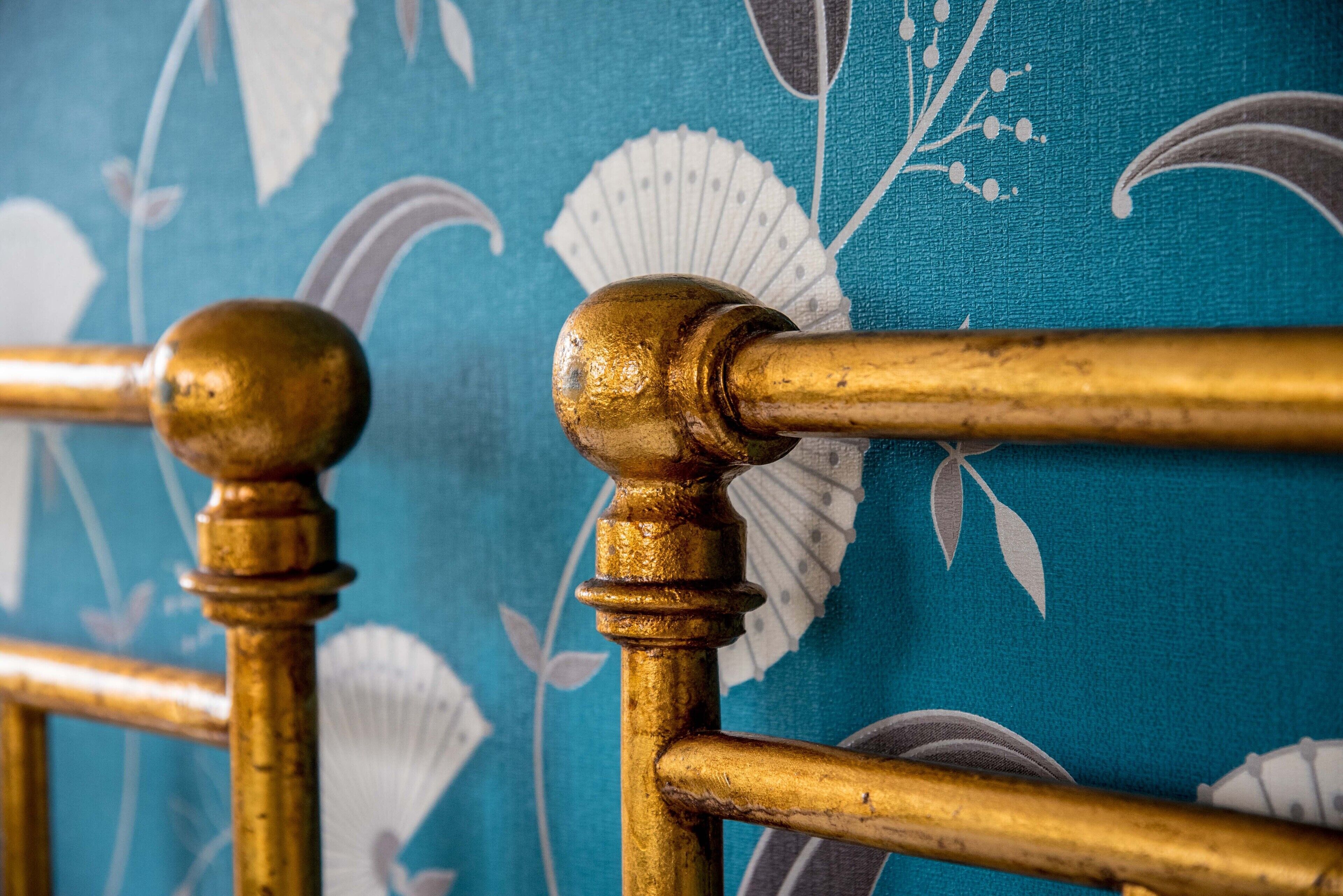 A close-up of a brass bed frame with a floral patterned fabric background.