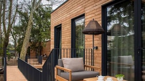 Una terraza de madera con un sofá, una mesa, una lámpara y vistas a árboles.
