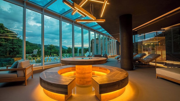 Un interior moderno con una mesa circular de madera en el centro, ventanas amplias que ofrecen vistas a la vegetación y una zona de estar con asientos.