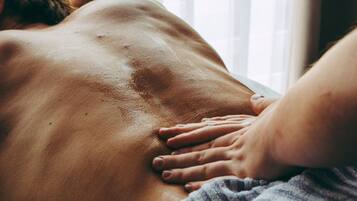 Eine Person erhält eine Rückenmassage in einem Raum mit Fenster und Jalousien.