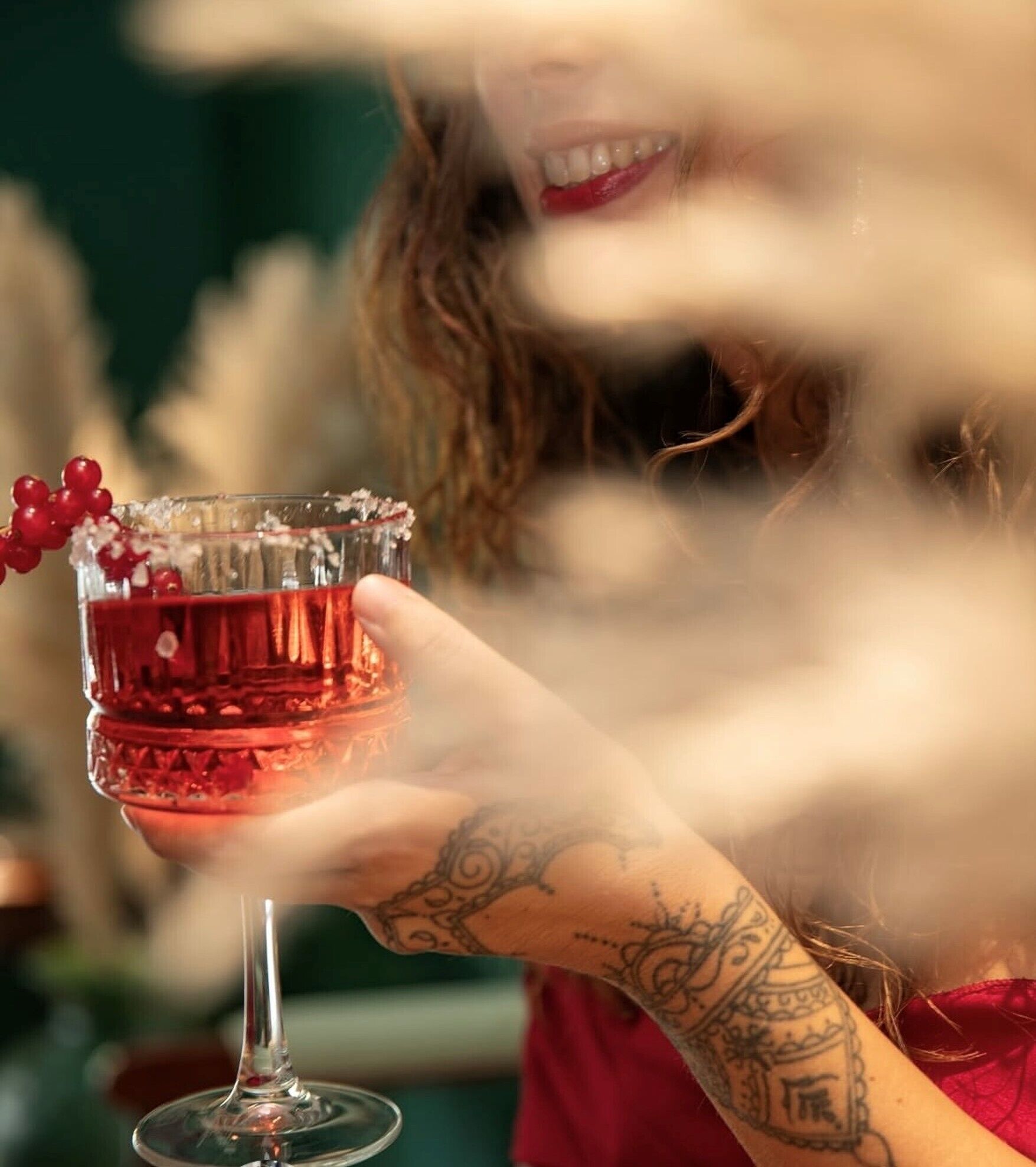 En person holder et glas med en rød drik, sandsynligvis en cocktail, med pynt.