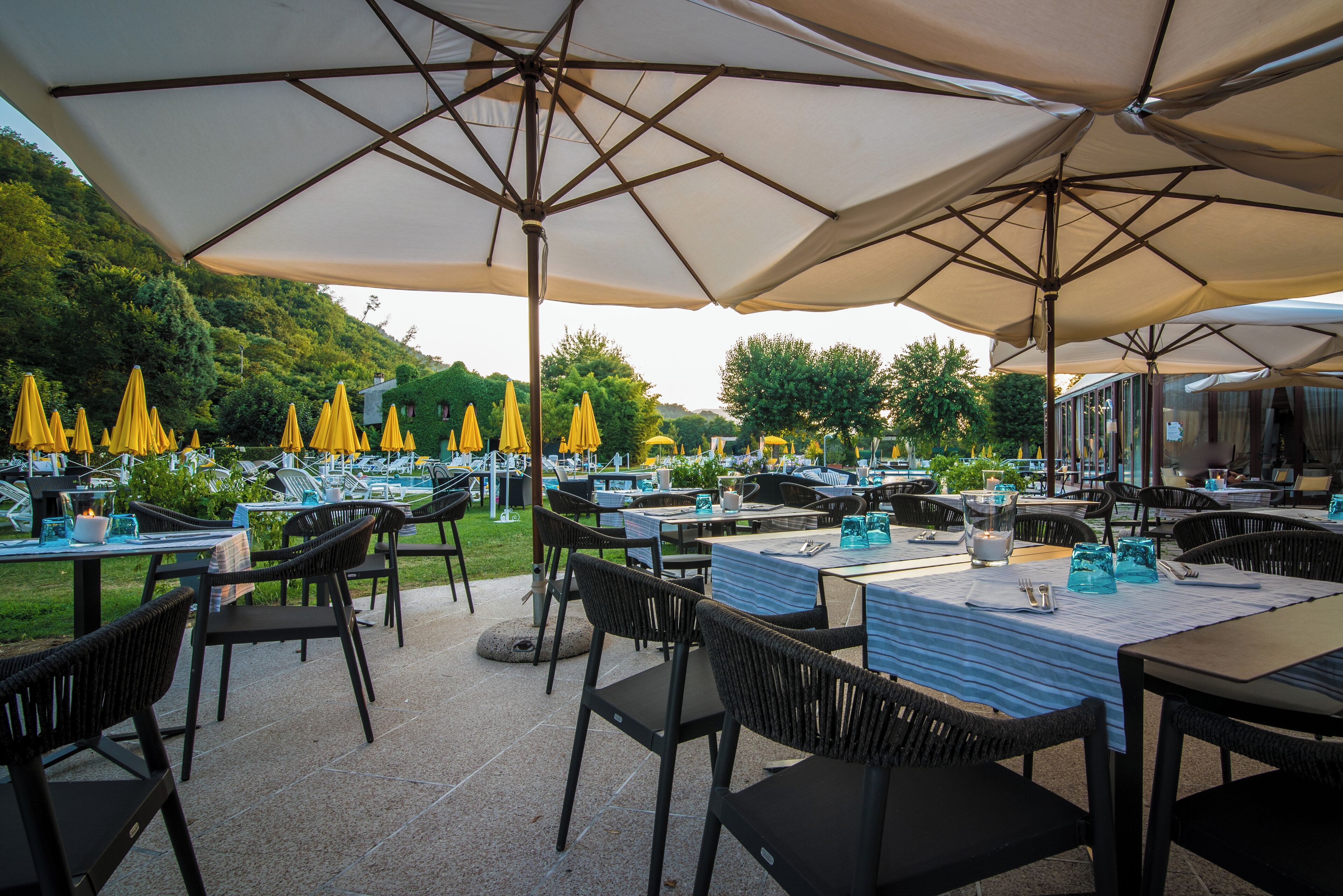 Un espace extérieur aménagé pour les repas, avec des tables et des chaises, des parasols, et une piscine en arrière-plan.