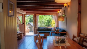 Un salon chaleureux avec un plancher en bois, un canapé, une table à manger avec des chaises et une grande fenêtre avec des rideaux.