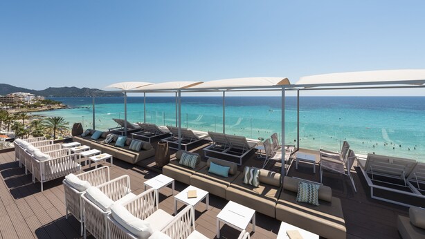 Un salon sur le toit, doté d’un espace extérieur avec des sièges et des parasols, offrant une vue sur la plage.