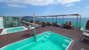 Un espace piscine sur le toit, avec une eau d’un bleu limpide, des chaises longues et un espace spa fermé par des parois de verre.