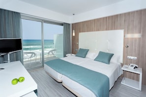 Une chambre d’hôtel moderne avec un grand lit, un bureau avec une télévision et une vue sur l’océan.