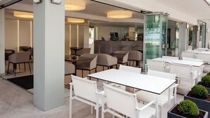 Un espace de restauration extérieur moderne, avec des tables et des chaises blanches, une cloison en verre et un éclairage d’ambiance.
