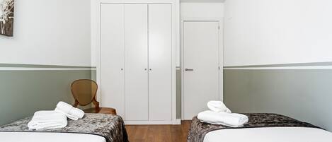 A hotel room with two beds, a wooden chair, a white door, and a painting on the wall.