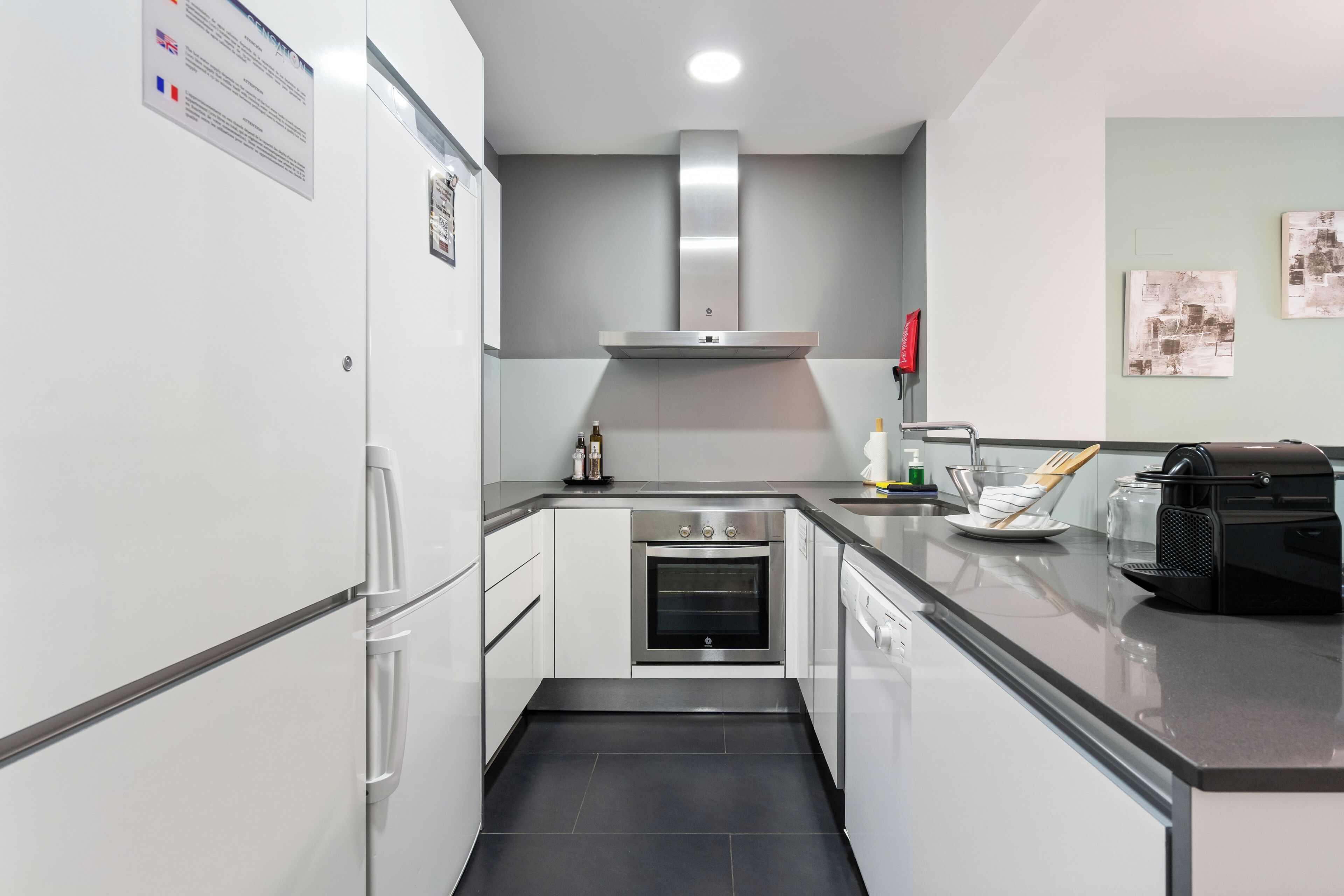A modern kitchen with white cabinets, a stainless steel oven, and a black coffee machine.