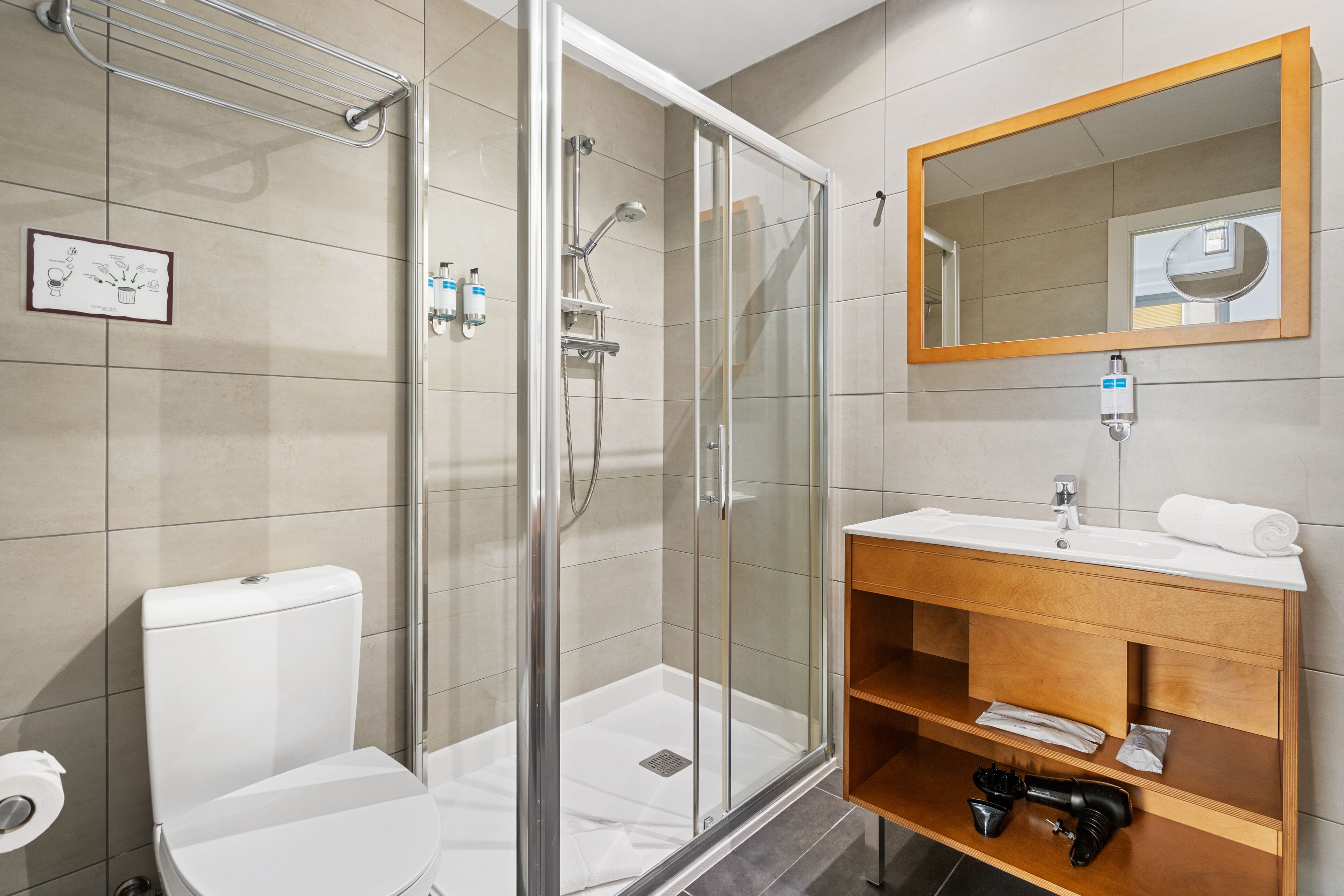 Ein modernes Badezimmer mit einer gläsernen Dusche, einer weißen Toilette, einem Holzkosmetikschrank mit Spiegel und einem Handtuchhalter.