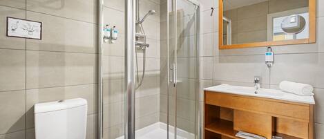 Ein modernes Badezimmer mit einer gläsernen Dusche, einer weißen Toilette, einem Holzkosmetikschrank mit Spiegel und einem Handtuchhalter.