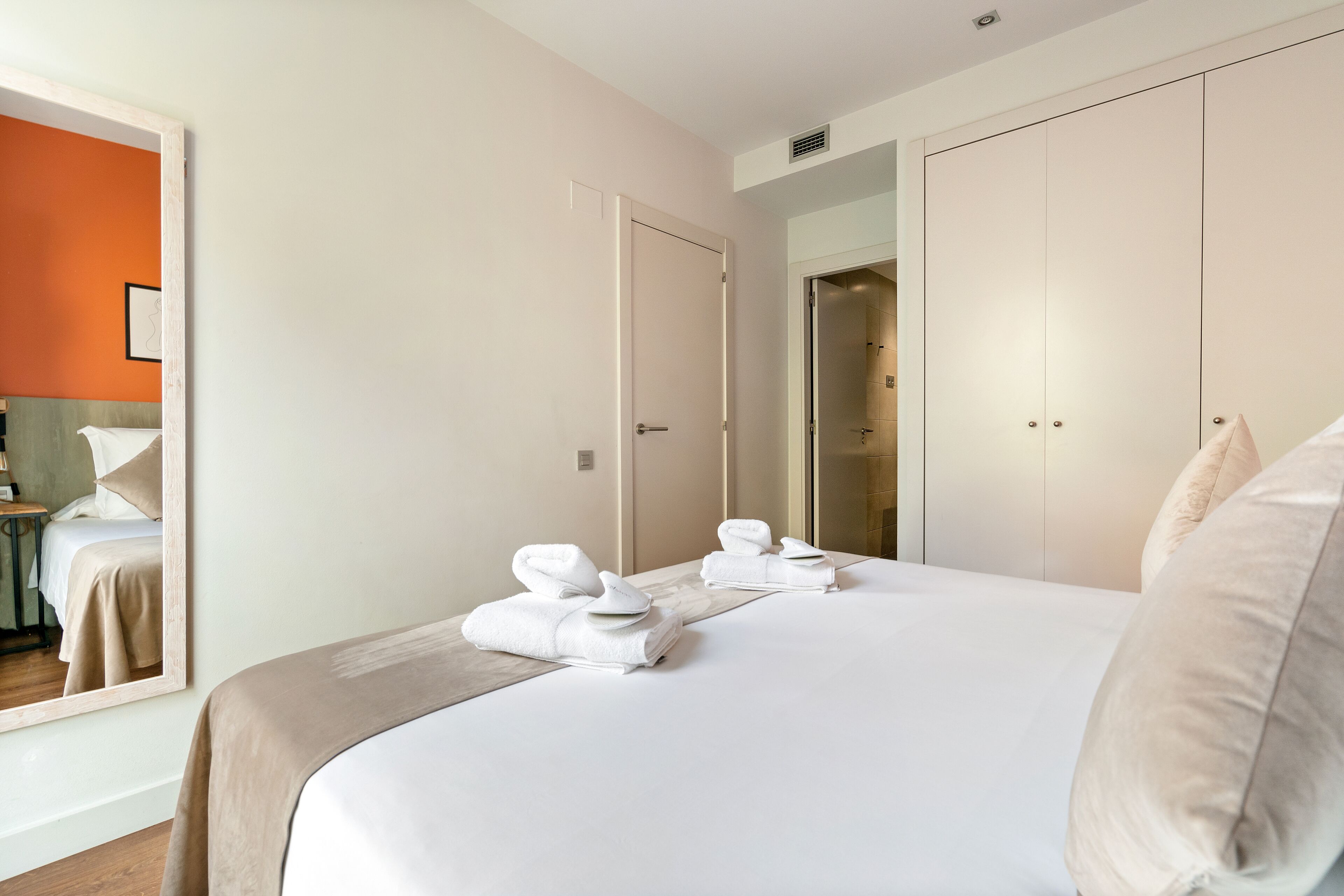 A hotel room with a large bed, two doors, a mirror, and a bathroom visible through an open door.