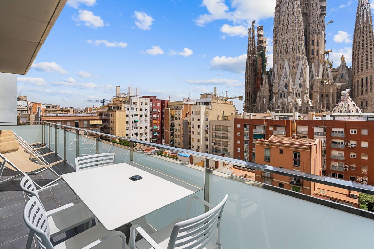 Un balcon doté d’une balustrade en verre, offrant une vue sur le paysage urbain, et mettant en valeur un bâtiment remarquable à l’architecture originale.