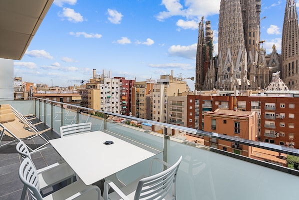 Un balcon doté d’une balustrade en verre, offrant une vue sur le paysage urbain, et mettant en valeur un bâtiment remarquable à l’architecture originale.