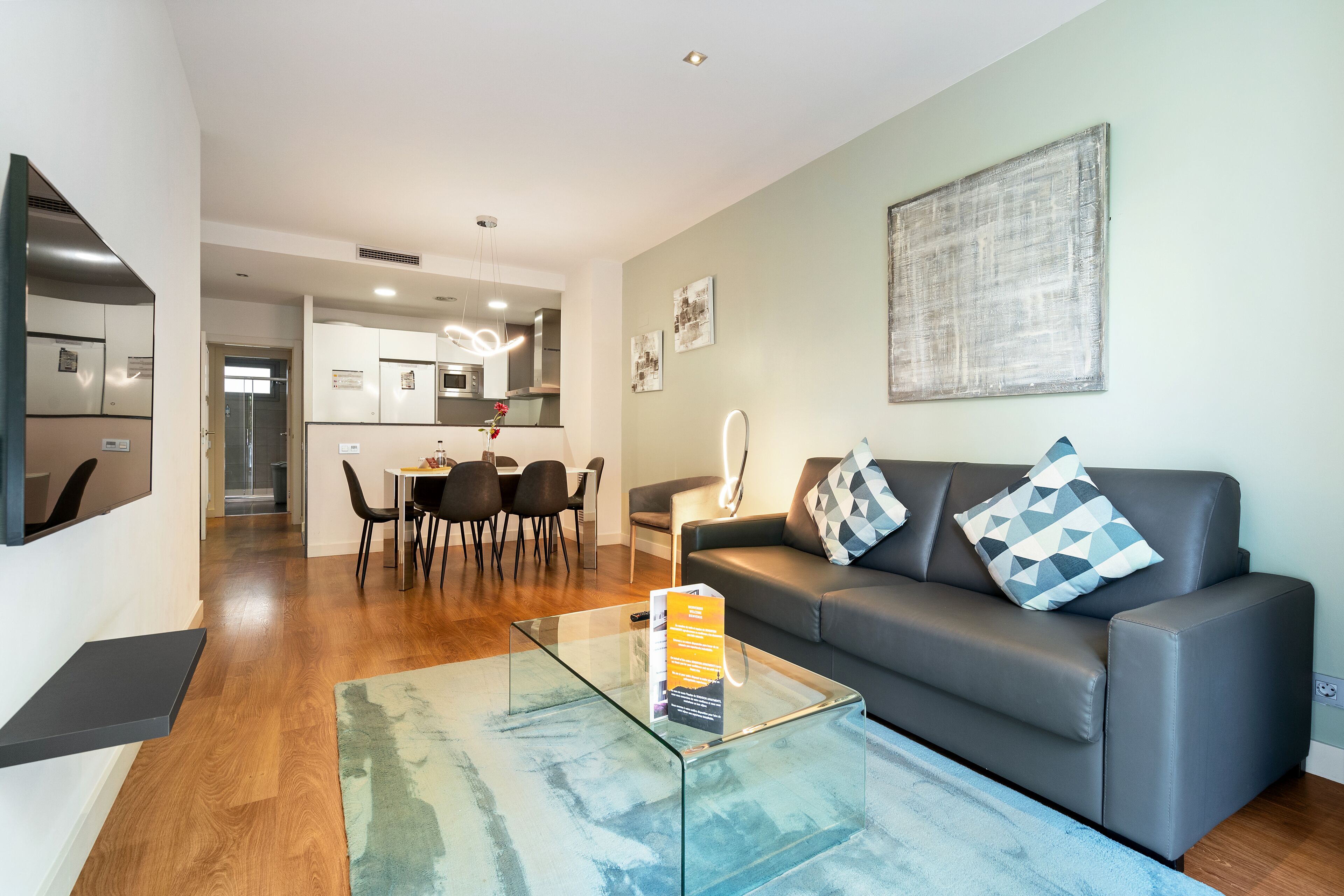 Un salon moderne avec une table basse en verre, un canapé gris et un coin repas à l’arrière-plan.