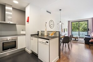 Eine moderne Küche mit integrierten Geräten, ein Essbereich mit Tisch und Stühlen sowie ein großes Fenster mit Blick ins Freie.