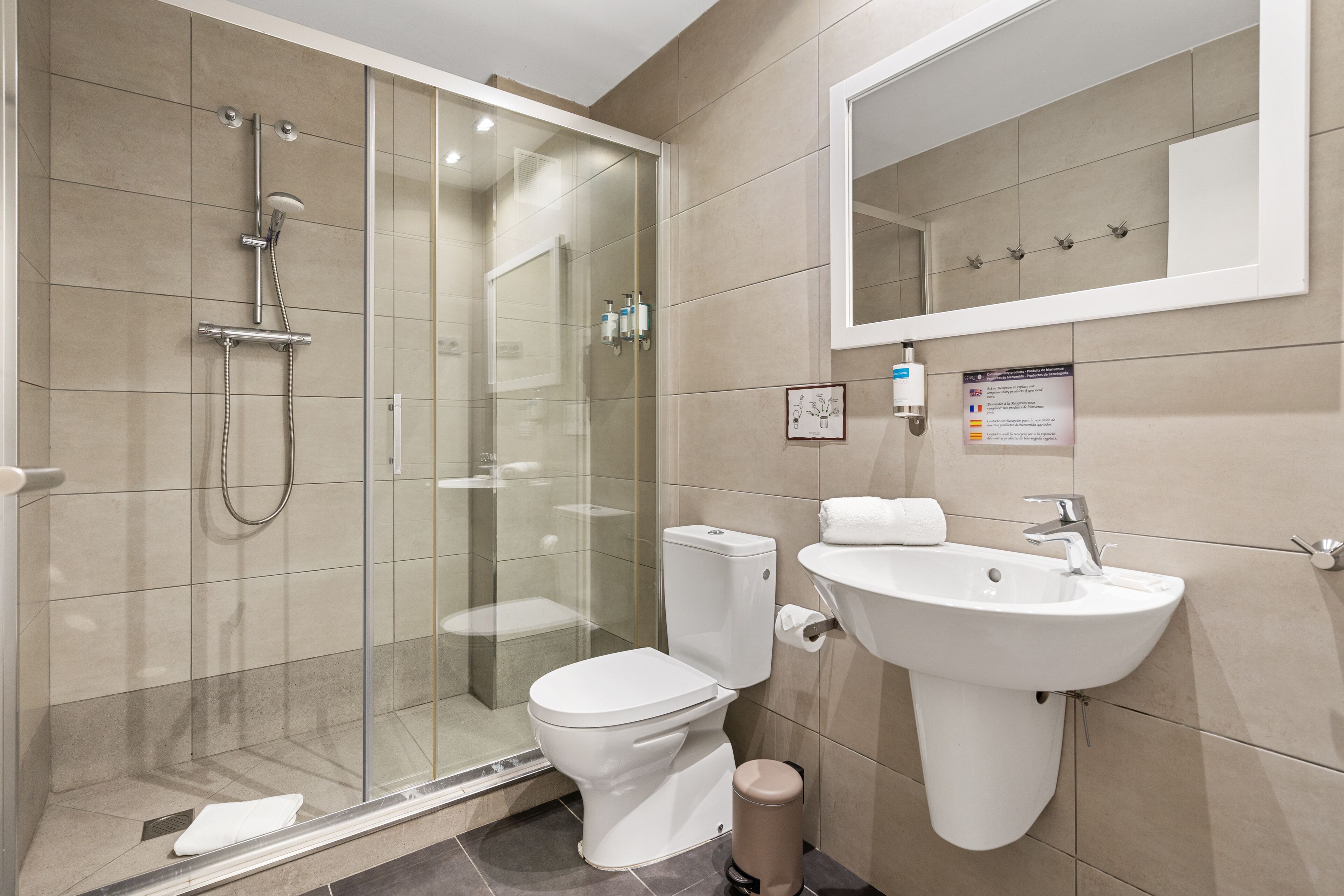 Une salle de bain moderne avec une douche à parois de verre, des toilettes blanches et un lavabo avec un miroir au-dessus.