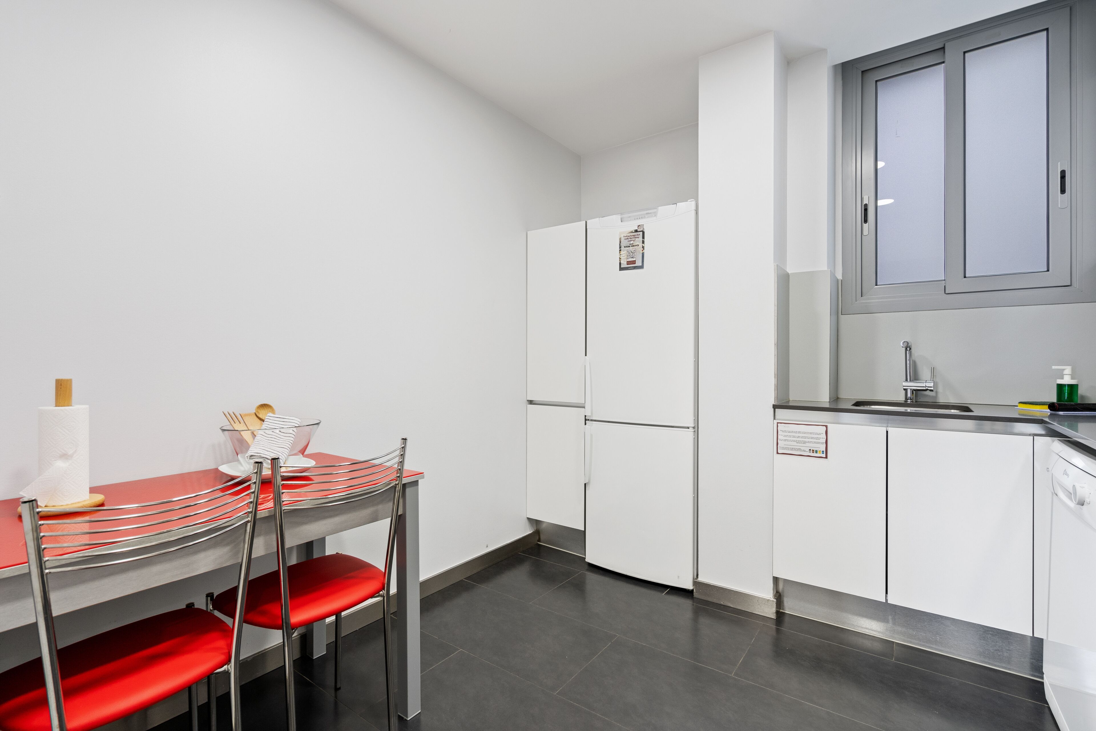 A compact kitchen with a dining area, white cabinets, and a stainless steel refrigerator.