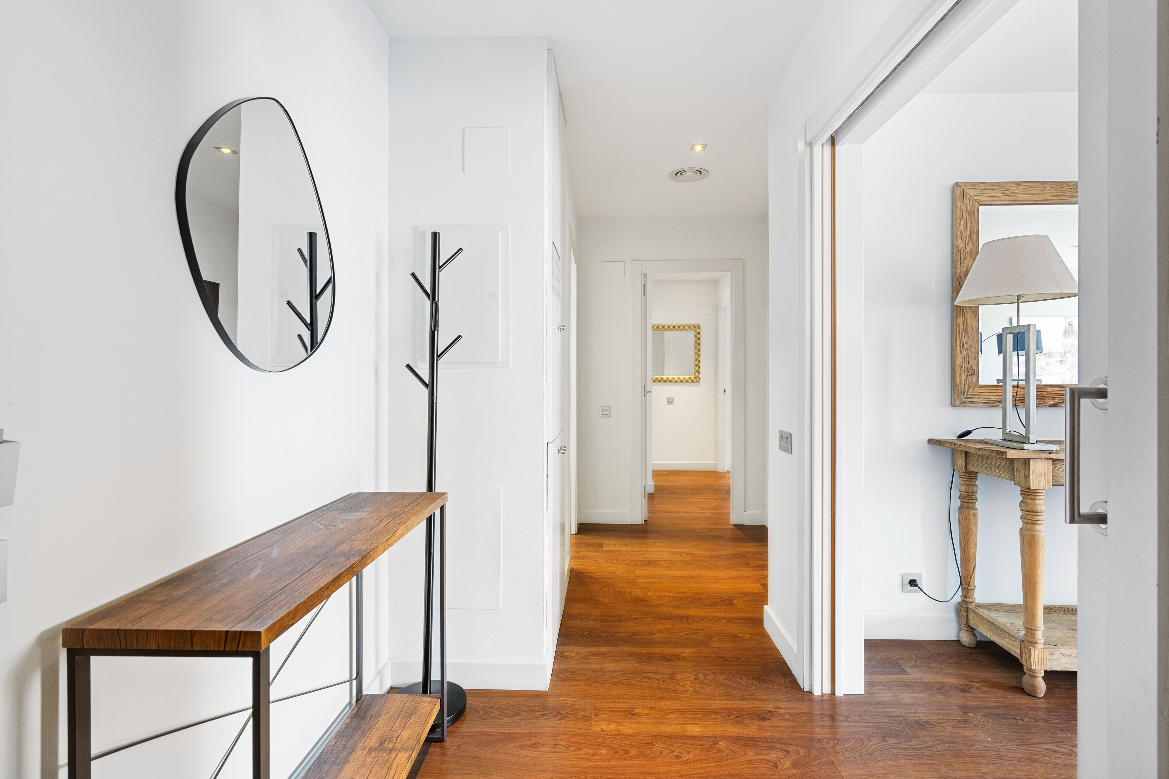 A hallway with a wooden bench, a coat rack, and a mirror on the wall.