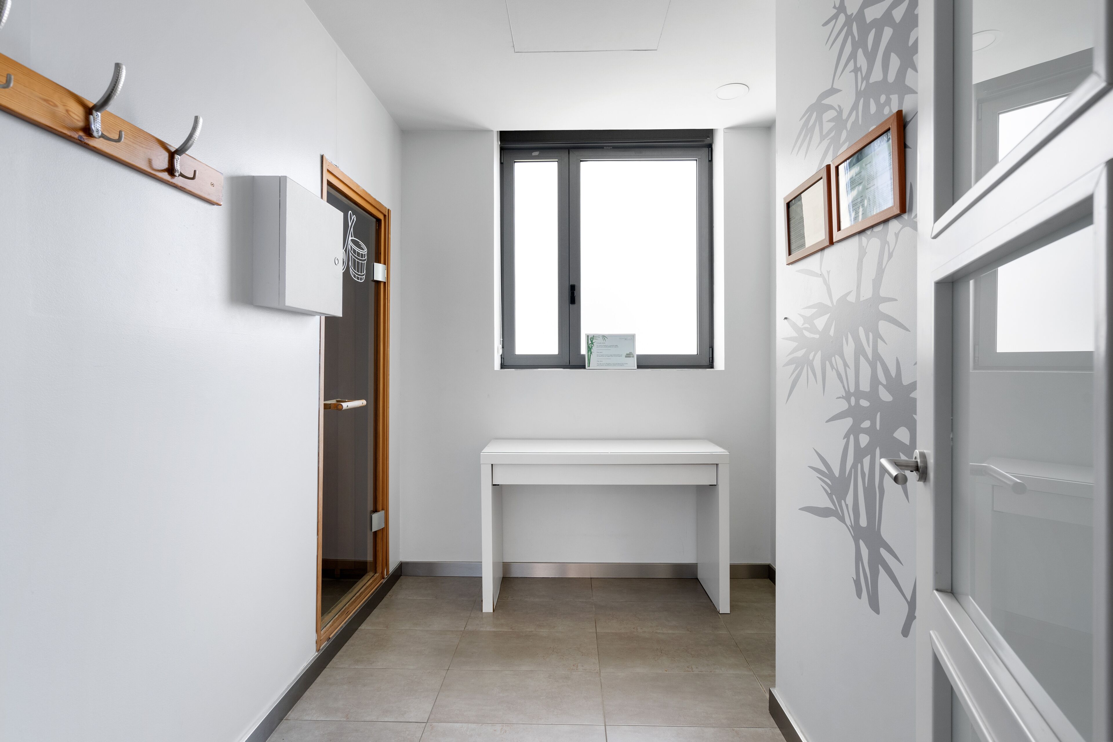 Un couloir avec un banc blanc, un porte-manteau, une porte avec une fenêtre et un climatiseur fixé au mur.