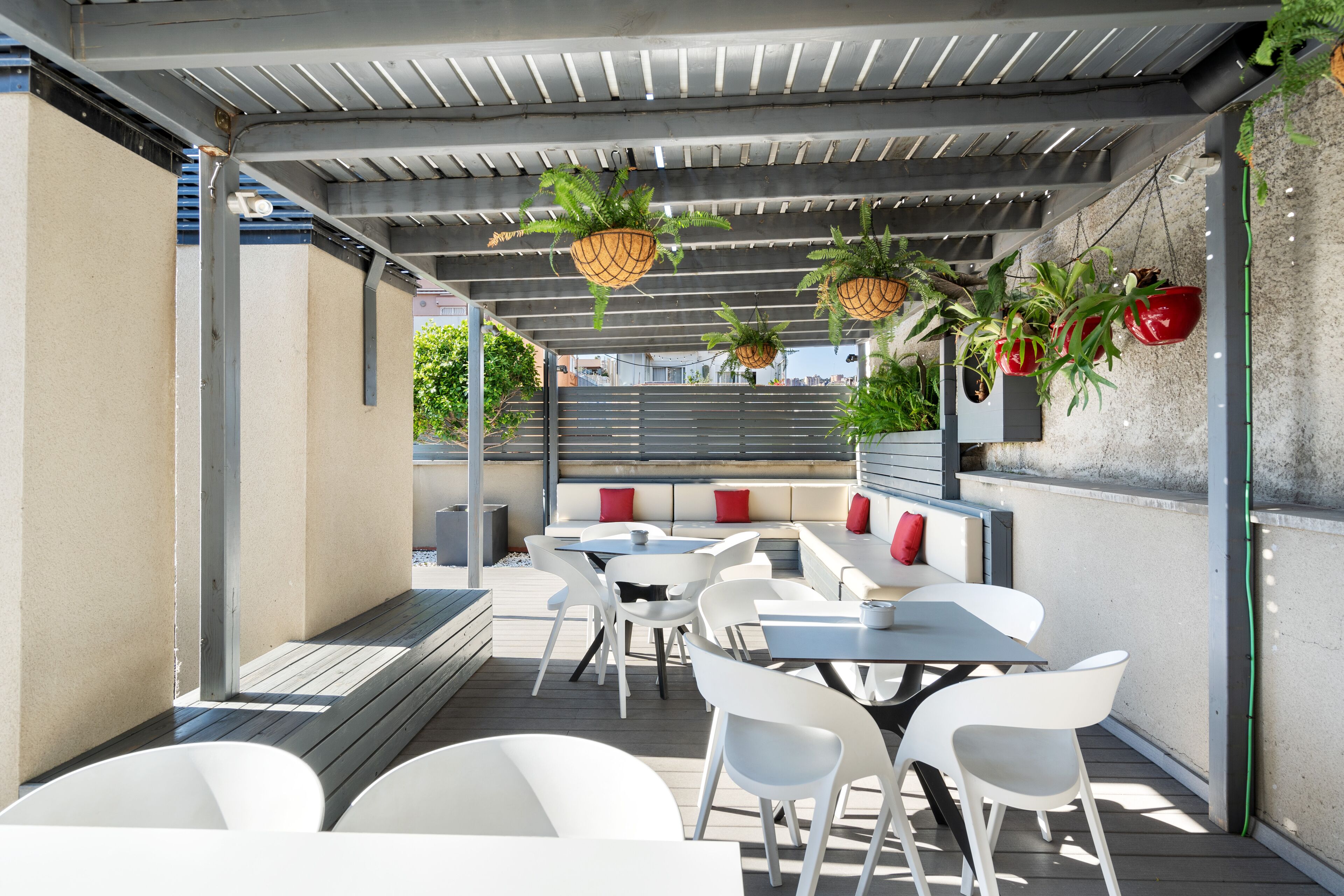 An outdoor patio with white tables and chairs, hanging planters, and a seating area with red cushions.