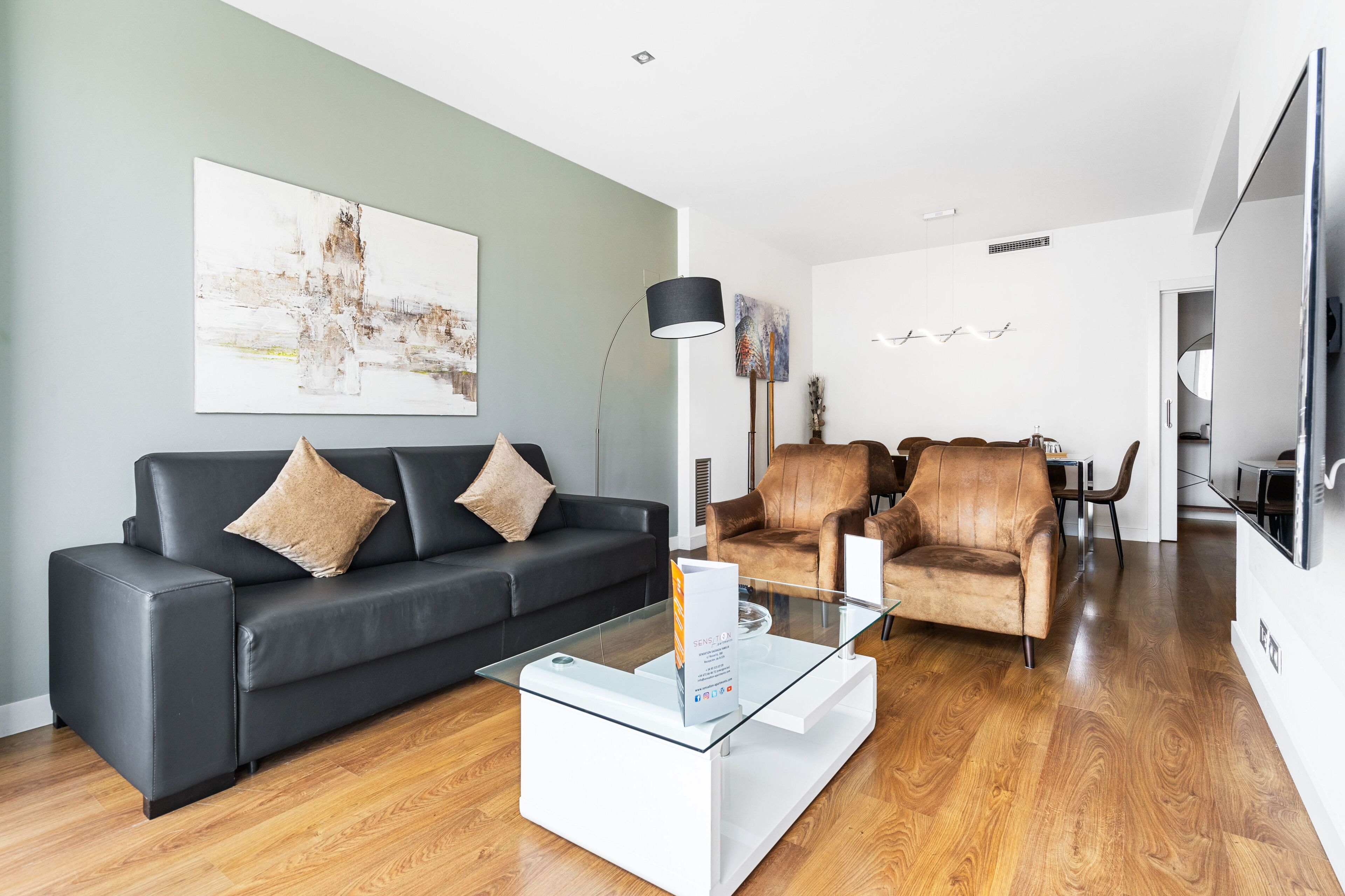 A modern living room with a black leather sofa, a glass coffee table, and a brown leather armchair.