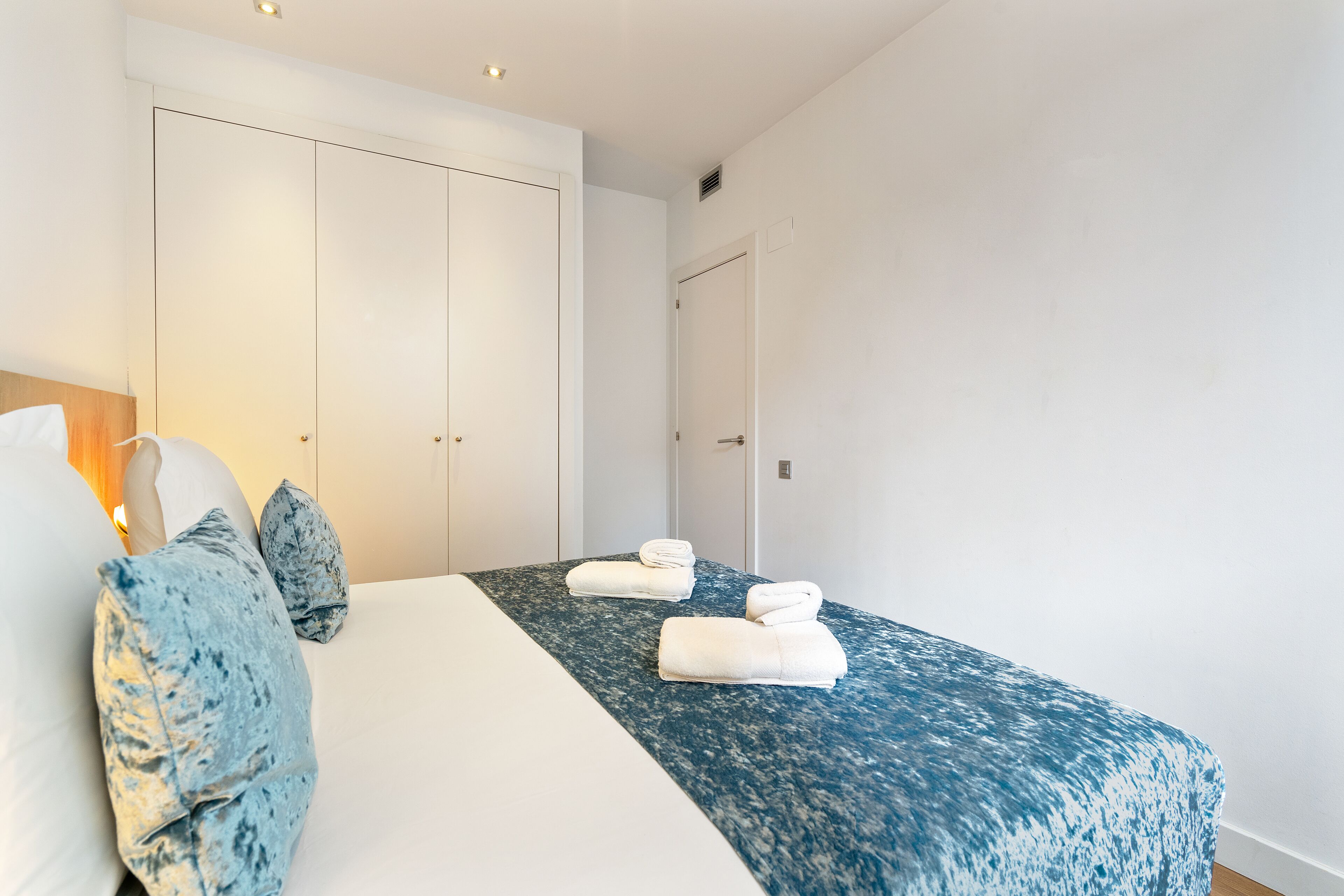 Ett hotellrum med en säng, två vita handdukar, ett blått, mönstrat överkast och en garderob.