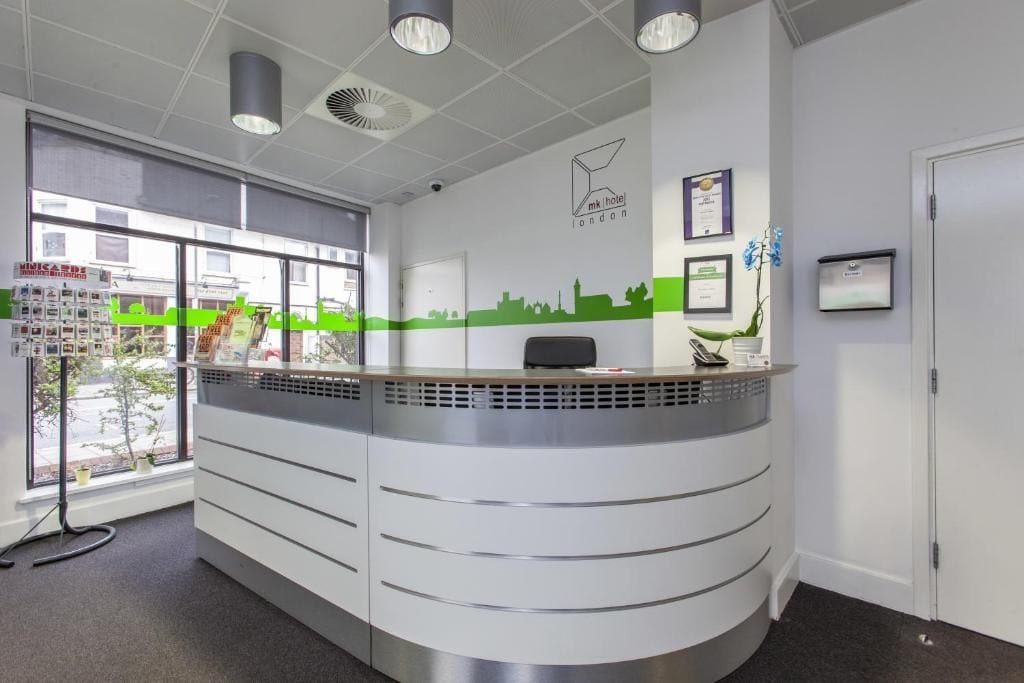 A reception desk with a cityscape mural, a framed certificate, and a potted plant.