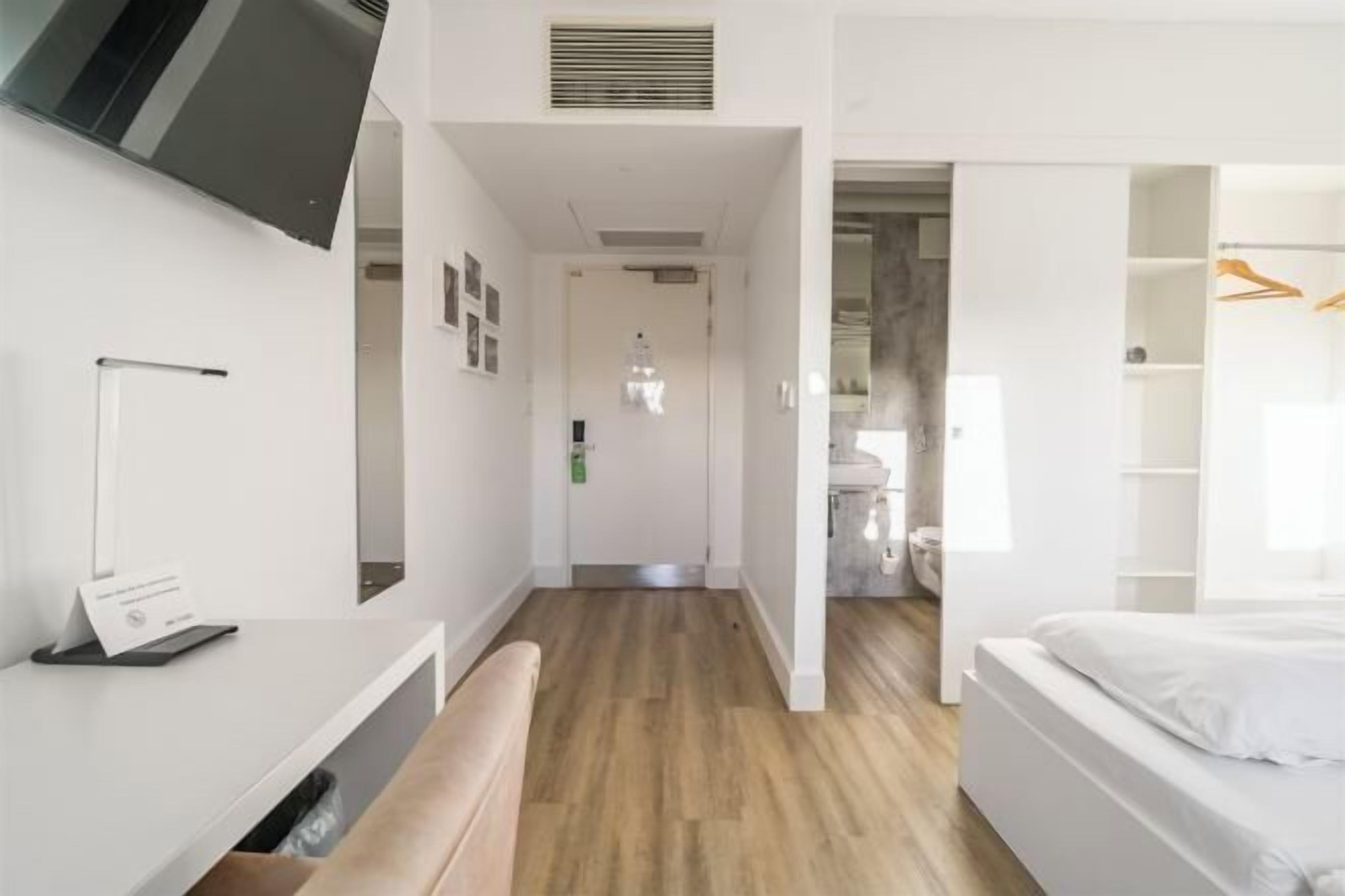 Une chambre d’hôtel moderne avec un plancher en bois, un lit, un bureau et une armoire.