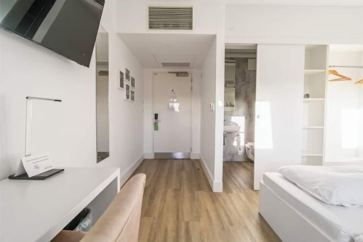 Et moderne hotelværelse med trægulv, seng, skrivebord og garderobeskab.