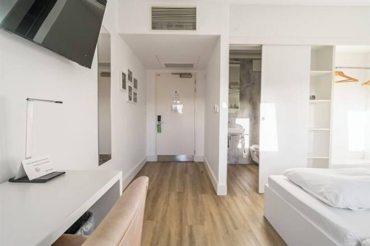 Quarto de hotel moderno com piso de madeira, uma cama, uma escrivaninha e um guarda-roupa.