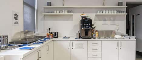 A modern kitchen with white cabinets, a coffee machine, and a buffet area with blue placemats.