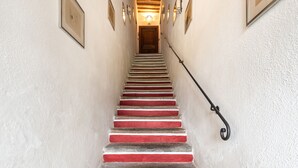 Una escalera con peldaños alternados en rojo y blanco, una puerta de madera en la parte superior y apliques de luz fijos a la pared.
