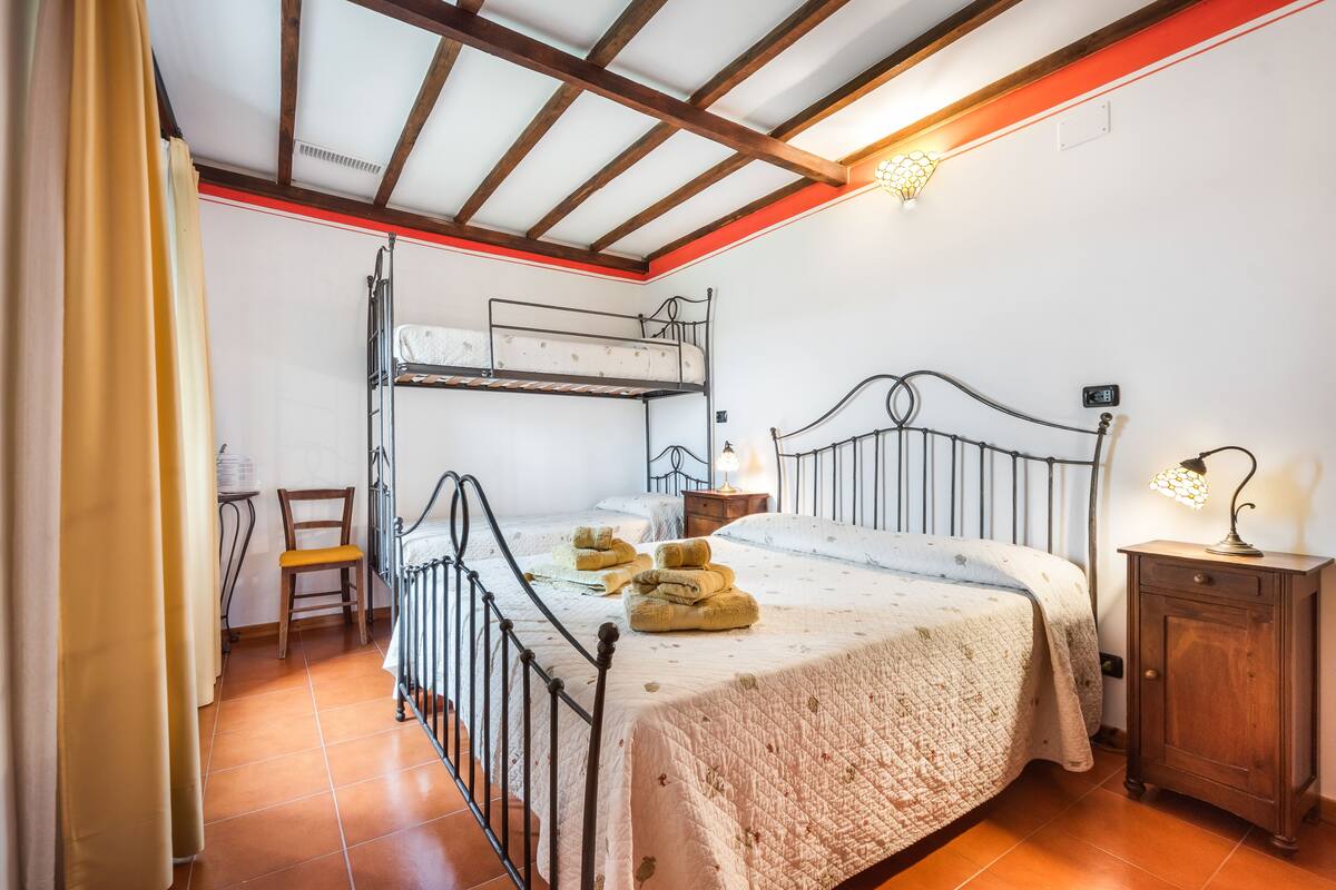 Un dormitorio con una cama litera, una cama individual, una mesita de noche de madera y una silla.