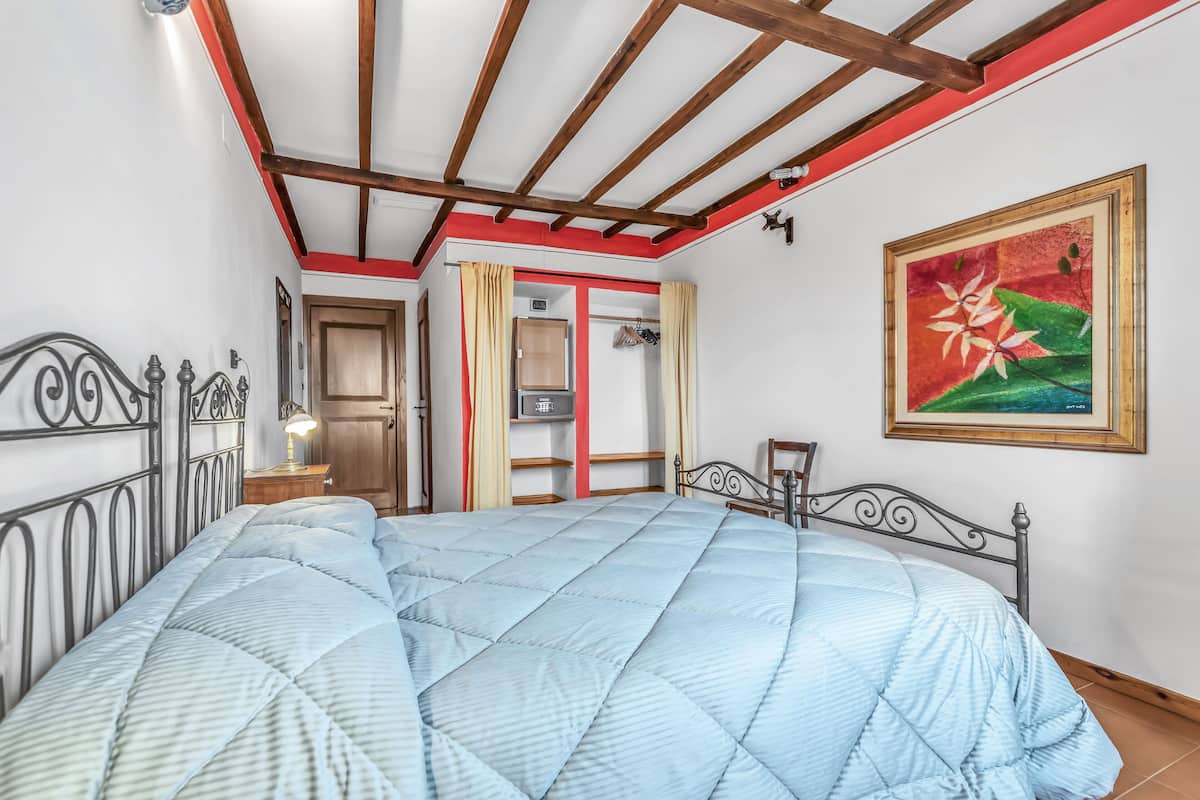Un dormitorio con cama, mesita de noche, lámpara, armario y un cuadro en la pared.