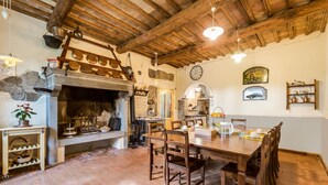 Una cocina rústica con chimenea de piedra, vigas de madera en el techo y un comedor con una gran mesa y sillas de madera.