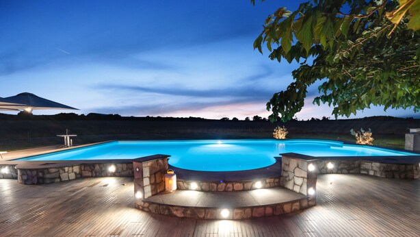 Una piscina con cubierta de piedra e iluminación, rodeada por un deck de madera y vistas al paisaje.
