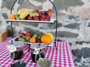 Una exhibición de frutas con un mantel a cuadros, dos frascos de conservas y un muro de piedra de fondo.