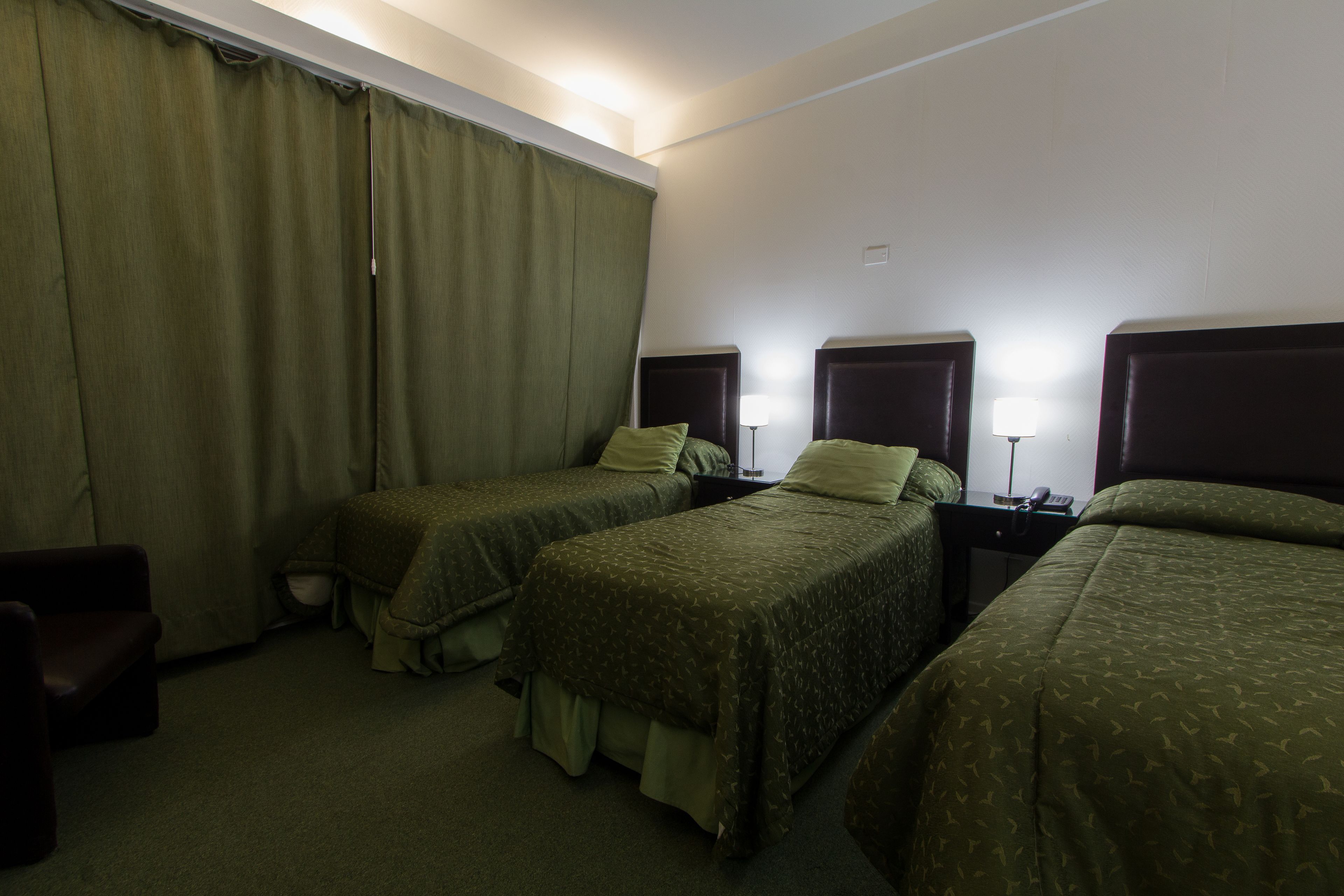 Une chambre d’hôtel avec deux lits simples, un petit bureau, une chaise et une grande fenêtre avec des rideaux.