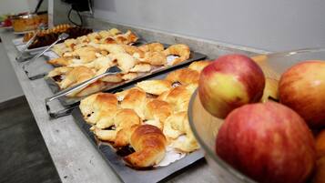 A buffet with trays of pastries and a bowl of apples.