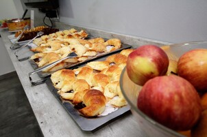 A buffet with trays of pastries and a bowl of apples.