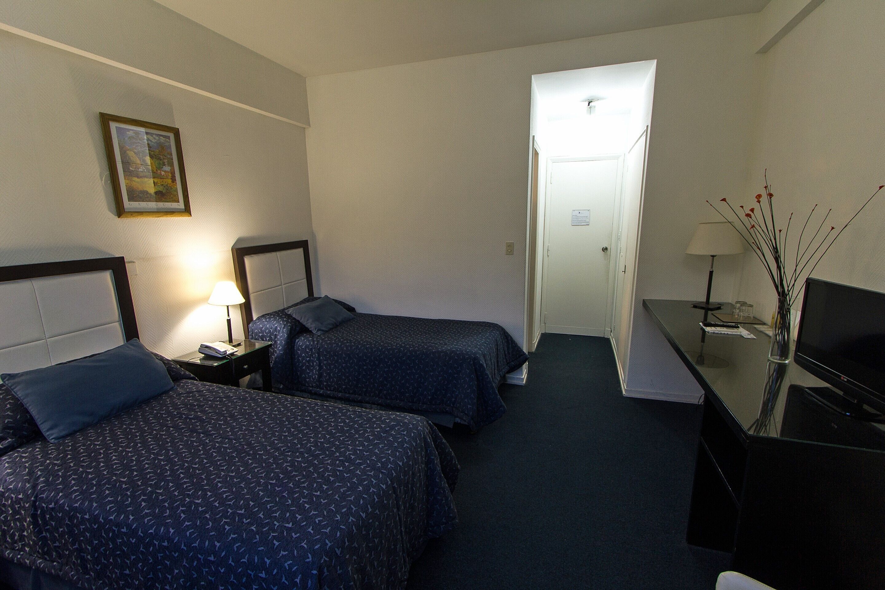A hotel room with two beds, a desk with a TV, and a lamp.