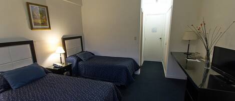 A hotel room with two beds, a desk with a TV, and a lamp.